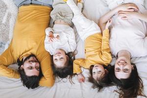 joven familia feliz con dos niñas en la cama en un hogar acogedor, vista desde arriba foto