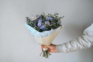 Young man in grey hoodie with bouqet of flowers in hands on grey background photo