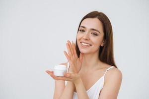 Beauty portrait of happy smiling woman with dark long hair put day nourishing moisturizer cream on clean fresh skin face and hands on the white background isolated photo