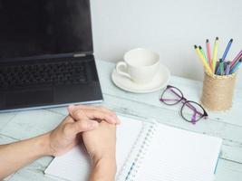 Hand on blank paper notebook with laptop and coffee and glasses on the desk workspace concept photo