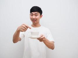hombre asiático camisa blanca señalar con el dedo la taza de café en la mano con una sonrisa feliz invitar concepto sobre fondo blanco aislado foto