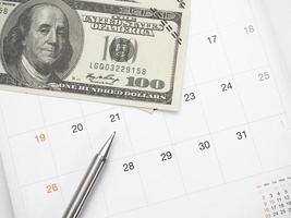 pluma de primer plano y dólar de dinero en la mesa del calendario foto