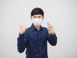 Portrait asian man wearing mask show fist up and holding infrared thermometer in hand white background photo