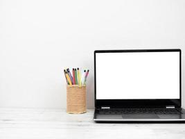 pantalla blanca de portátil con caja de lápices en el espacio de trabajo de la mesa foto