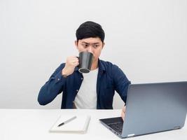 Man drinking coffee cup serious emotion and looking at laptop on the desk photo