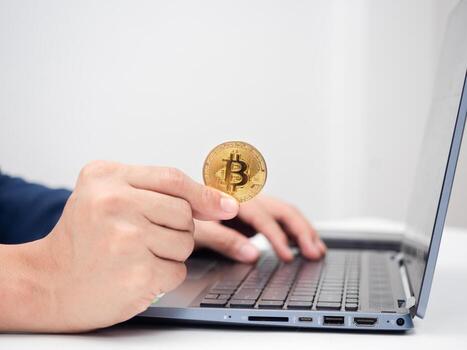 Close up man hand holding gold bitcoin and using laptop on the table photo