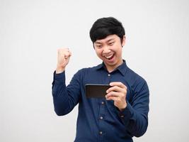 hombre asiático jugando en el teléfono móvil sintiéndose feliz mostrar puño arriba foto
