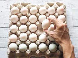 Hand holding duck eggs on group duck eggs in carton box on white wood table with nature shadow and light photo