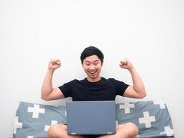 Asian man looking at laptop and show fist up feeling happy in bedroom photo