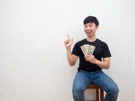 hombre asiático sosteniendo dinero en la mano y señalando con el dedo el espacio de la copia sonrisa alegre y feliz concepto de hombre rico foto