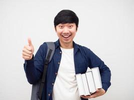 hombre asiático con mochila escolar sosteniendo libros pulgar arriba cara alegre fondo blanco foto