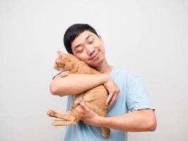 hombre asiático abraza a su gato color naranja en la mano sintiéndose feliz foto