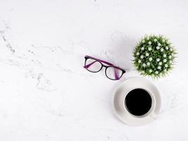 Coffee cup glasses and flower vase on white marble background top view copy space photo