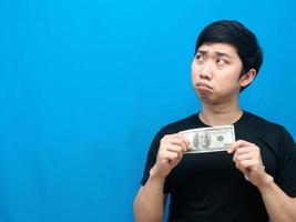 hombre asiático sosteniendo dinero en la mano sintiendo una emoción triste mirando el espacio de la copia concepto de hombre pobre foto