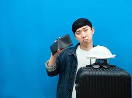 hombre gesto sin dinero con billetera sintiéndose triste con equipaje fondo azul foto