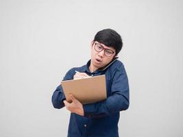 Asian man wearing glasses busy and writing on document board in hand and talking with mobile phone white background photo