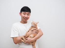 un hombre asiático lleva un gato naranja en la mano alegre y feliz con un fondo aislado blanco foto