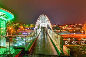 el puente de la paz en tbilisi, un puente peatonal sobre el río mtkvari en tbilisi, georgia iluminado por la noche. foto