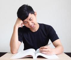 joven con bolígrafo serio y siente tensión con problema toca su cabeza a mano con el libro en el escritorio en blanco aislado foto