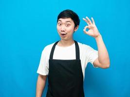 Asian man wearing apron black make hand ok blue background photo