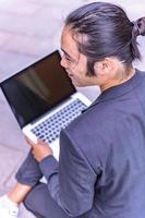 asian male freelancer walking near business center holding phone, smiling reading news, successful businessman photo