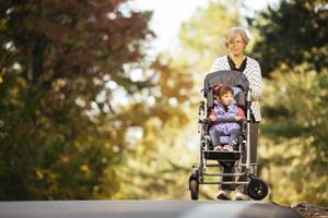 Happy senior lady pushing wheel chair and children. Grandmother and kids enjoying a walk in the park. Child supporting disabled grandparent. Family visit. Generations love and relationship photo