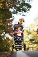 Happy senior lady pushing wheel chair and children. Grandmother and kids enjoying a walk in the park. Child supporting disabled grandparent. Family visit. Generations love and relationship photo