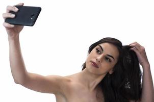 imagen de una hermosa mujer morena riéndose mientras toma una foto selfie en un celular aislado sobre fondo blanco