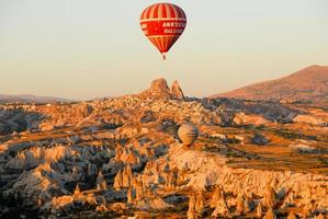 Goreme, Turkey - September 21, 2007 -  Hot air balloon rising over Goreme village, Turkey at sunrise. Rural Cappadocia landscape. Stone houses in Goreme, Cappadocia. Countryside lifestyle. photo