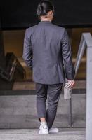 asian male freelancer walking near business center holding phone, smiling reading news, successful businessman photo