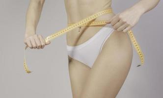 Concept of healthy eating. Young girl with perfect waist with a measuring tape in hands photo