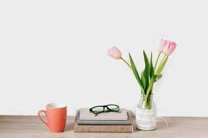 un ramo de tulipanes rosas de flores de primavera en un jarrón se encuentra en el escritorio junto a cuadernos con gafas y una taza de té. copie el espacio
