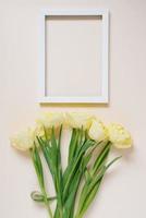 Bouquet of yellow spring tulips on the table, next to an empty white photo frame with copy space. Flat lay