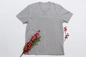 Close up grey blank template t shirt with copy space and Christmas Holiday concept. Top view mockup t-shirt and red holidays decorations on white background. Happy New Year accessories. Xmas outfit photo
