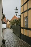 Detail of the street lamp with ornaments hanging on the yellow wall of the old house in the empty street, with granite road, of the oldest Denmark village Ribe with the overcast sky in the background photo