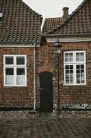 Narrow wooden door between old brick houses with white framed windows with the street lamp and stone road in front of them during the autumn afternoon after the rain in the oldest Denmark village Ribe photo