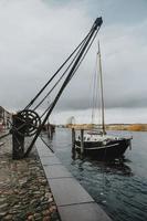 viejo velero en el río inundado en el puerto de la ciudad de ribe en dinamarca con la vieja grúa del puerto en frente durante el día nublado de otoño en orientación vertical foto