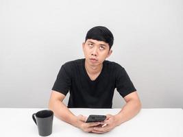 Man holding mobile phone at table feeling bored looking up photo