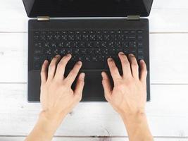 mano en el teclado de la computadora portátil en la vista superior de la mesa de madera foto