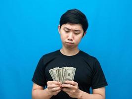 Asian man looking at money in his hand and feeling doubt blue background photo