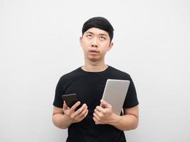 Asian man holding tablet with mobile phone feeling bored looking above photo