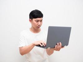 camisa blanca de hombre asiático sostenga la computadora portátil y toque el teclado con cara seria sobre fondo blanco foto