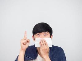 un hombre enfermo asiático cierra la nariz con un tejido que señala con el dedo el fondo blanco foto