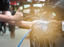 sujetar con la mano y con el pulgar hacia arriba el enchufe del vehículo de carga eléctrica y la luz de bengala para recargar la batería del coche energía de energía limpia de color negro para el concepto futuro foto