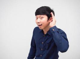 hombre asiático posando escuchando algo con la mano en su oreja fondo blanco foto