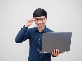 hombre asiático con anteojos sosteniendo una laptop con una sonrisa feliz, con cara de confianza, fondo blanco foto