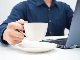 Close up hand holding coffee cup on the table workplace,Crop shot of man using laptop for working and holding coffee cup photo