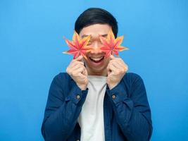 Cheerful man holding maple leaf close his eyes blue background photo