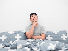 Asian man sitting on the bed gesture thinking about something looking up