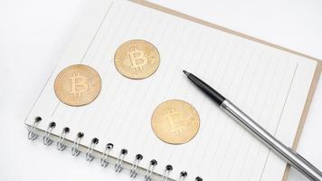 Bitcoin with pen on blank page notebook top view photo